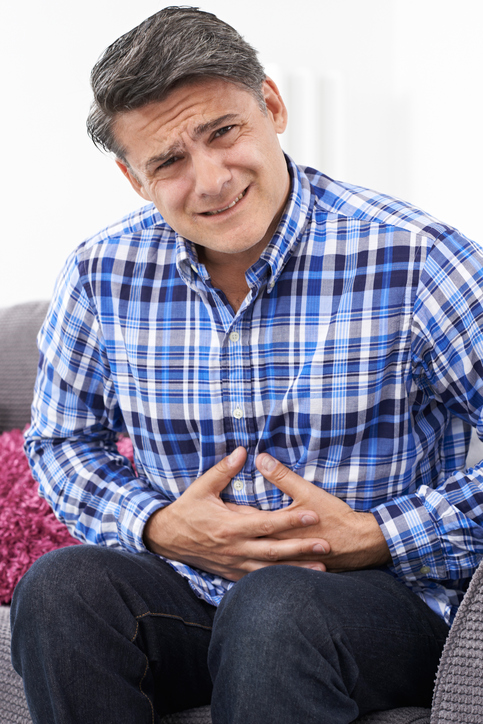 IBS - l'homme a des douleurs abdominales, des crampes, se tient l'abdomen, chemise bleue à carreaux, assis sur le canapé.