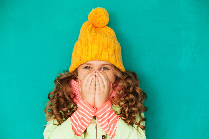 La petite fille est habillée et se couvre le visage avec ses mains.