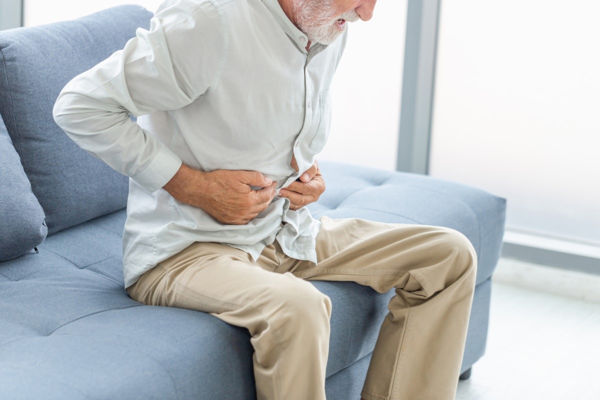 Une personne âgée souffre de douleurs abdominales - elle est en position couchée et se tient l'abdomen avec les mains.