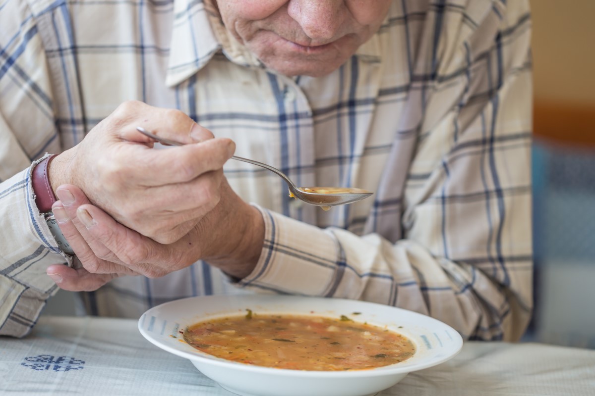 Un homme mange de la soupe et tient sa main contre les tremblements de la maladie de Parkinson