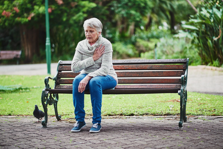 Une femme âgée est assise sur un banc et souffre de problèmes cardiaques.