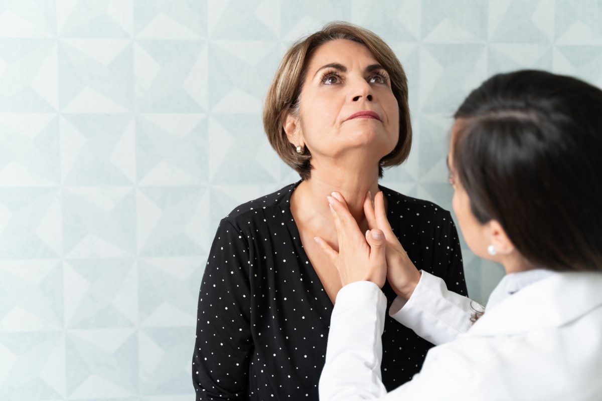 Médecin palpant la glande thyroïde, femme âgée assise en face