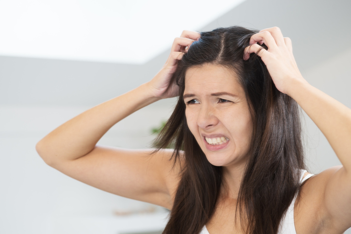 Une femme a des problèmes de cheveux, des pellicules, des démangeaisons du cuir chevelu et se gratte la tête avec les mains.