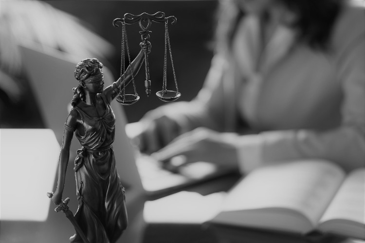 une femme assise à une table avec un livre devant elle et une statue de la justice au premier plan sur la table