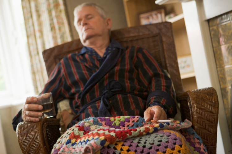 un grand-père endormi dans un fauteuil recouvert d'une couverture, un verre d'alcool et une cigarette à la main