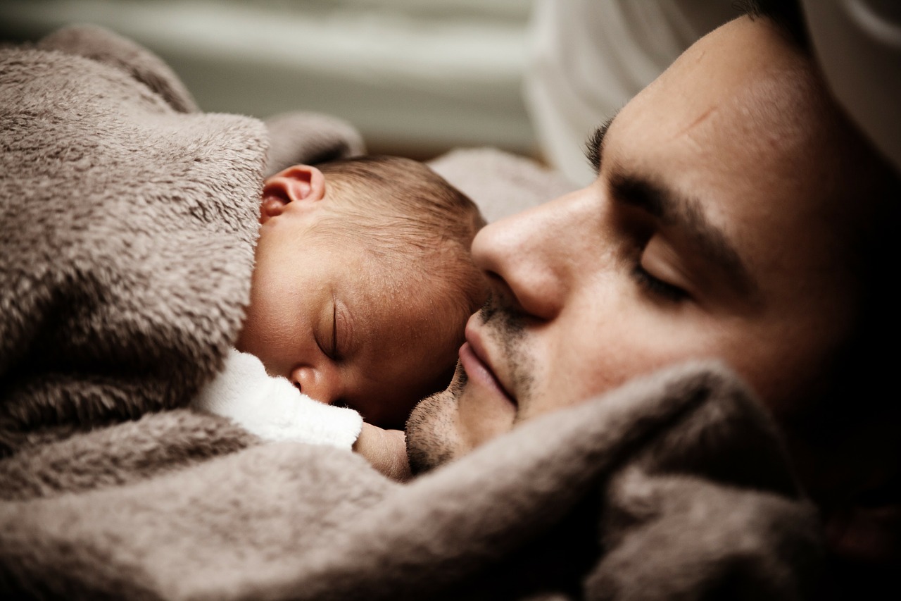 le bébé dort à côté de son père sous une couverture brune