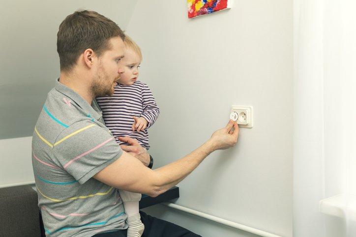 Le père tient un petit enfant dans ses bras et ferme la prise avec une fiche électrique.