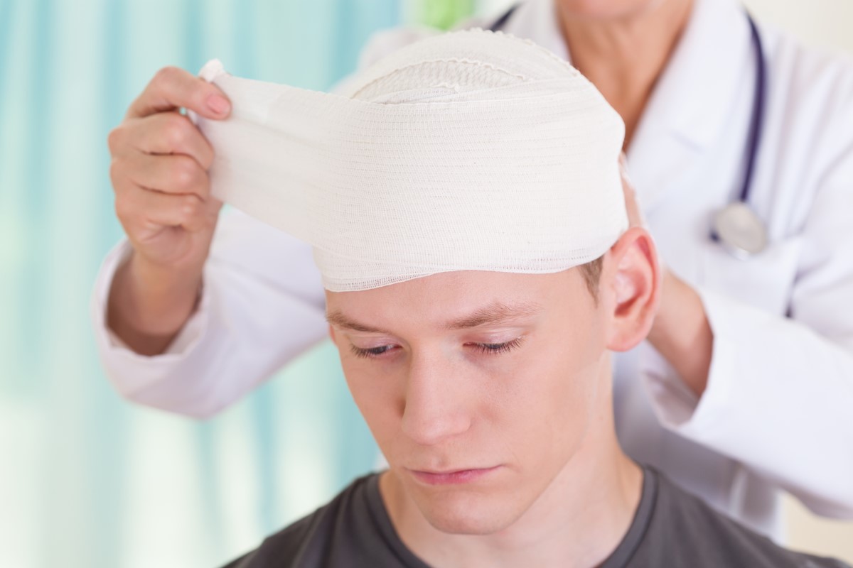 Maux de tête après un accident, tête bandée, un médecin traite un garçon souffrant d'un traumatisme crânien