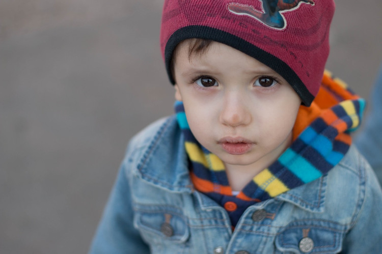 un enfant vêtu d'une veste bleue et coiffé d'une casquette rouge regarde dans l'objectif