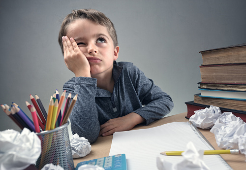 un écolier assis à son bureau, réfléchissant à quelque chose, avec un cahier, du papier, des crayons sur son bureau