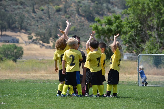 Enfants en maillots jaunes sur le terrain de football, en train de s'amuser en groupe avec leur entraîneur.