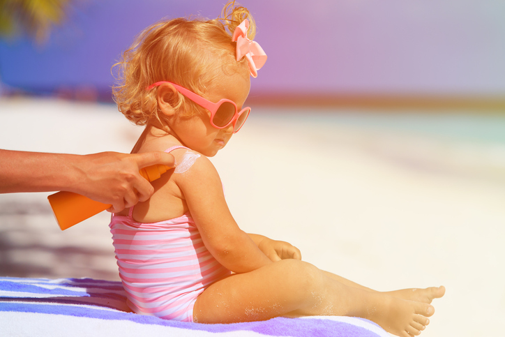 Un enfant prend un bain de soleil, sa mère lui applique de la crème solaire.