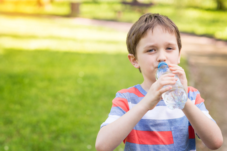 Garçon buvant de l'eau dans une bouteille, avec de l'herbe verte en arrière-plan