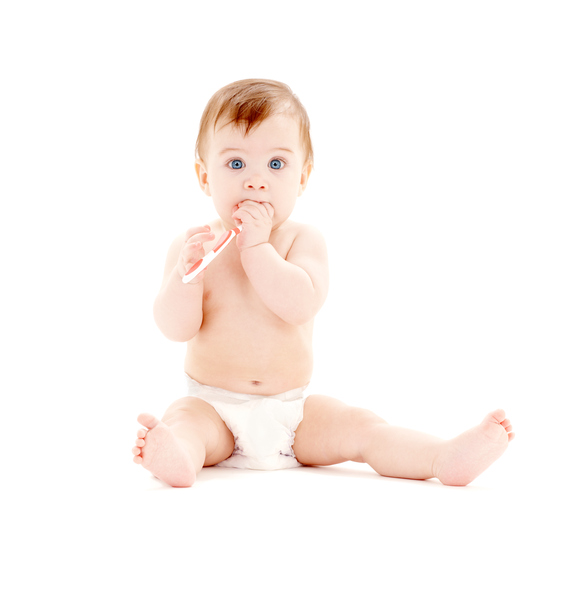 Un petit enfant en couche est assis, avec une brosse à dents dans les mains, qui est dans sa bouche.