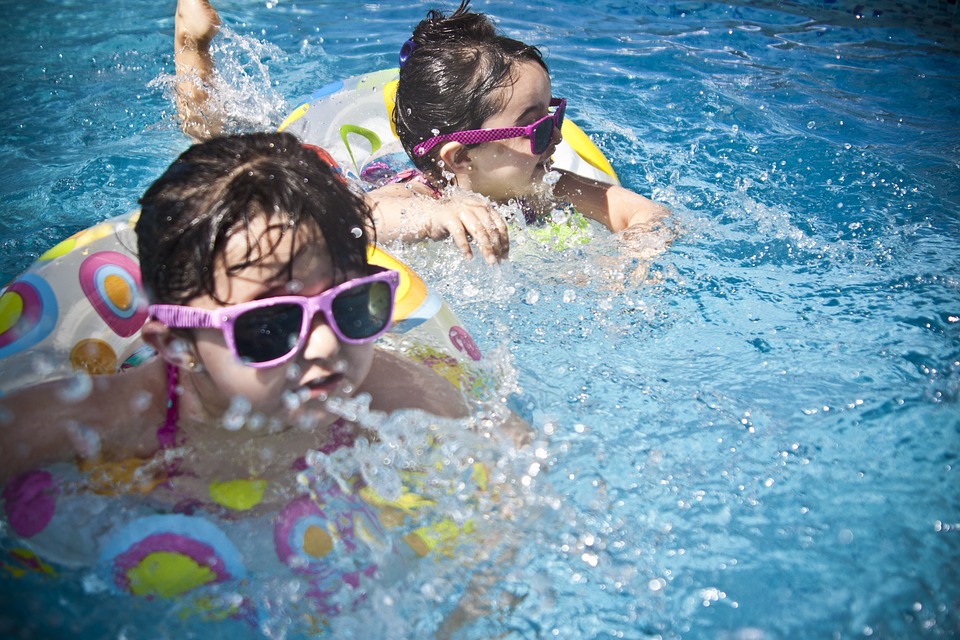 Deux enfants nagent dans l'eau. Ils portent des lunettes de soleil à monture rose. Ils sont sur des vélos flottants.