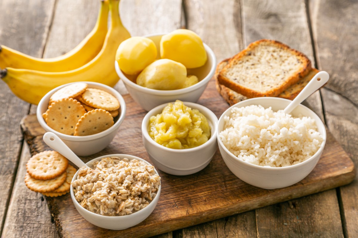 Exemple de régime alimentaire approprié en cas de diarrhée aiguë : riz, pommes de terre, bananes, crackers, crackers, dans des bols et sur une planche à découper en bois.