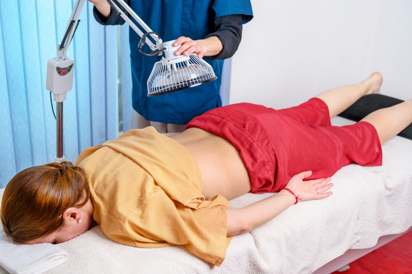 Une femme est allongée sur un lit et un homme place une lampe biologique sur sa zone sacrée.