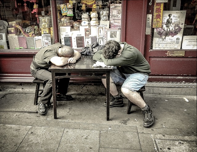 Deux hommes dorment à une table à l'extérieur du magasin. C'est un vieux magasin.