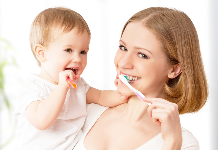 Une mère se brosse les dents avec son enfant dans les bras.