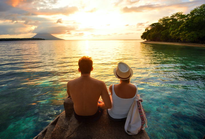 couple assis sur un rocher au bord de la mer au lever du soleil