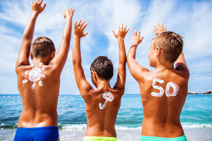 Crème solaire pour enfants avec OF 50, les enfants sont sur la plage au bord de la mer et s'amusent, ils ont les mains en l'air