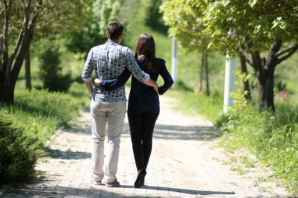 Couple marchant sur un sentier naturel, se tenant par la taille. Arbres verts, herbe verte.