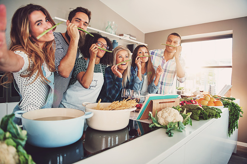 Des personnes sourient en préparant le repas. Elles sont derrière le fourneau.