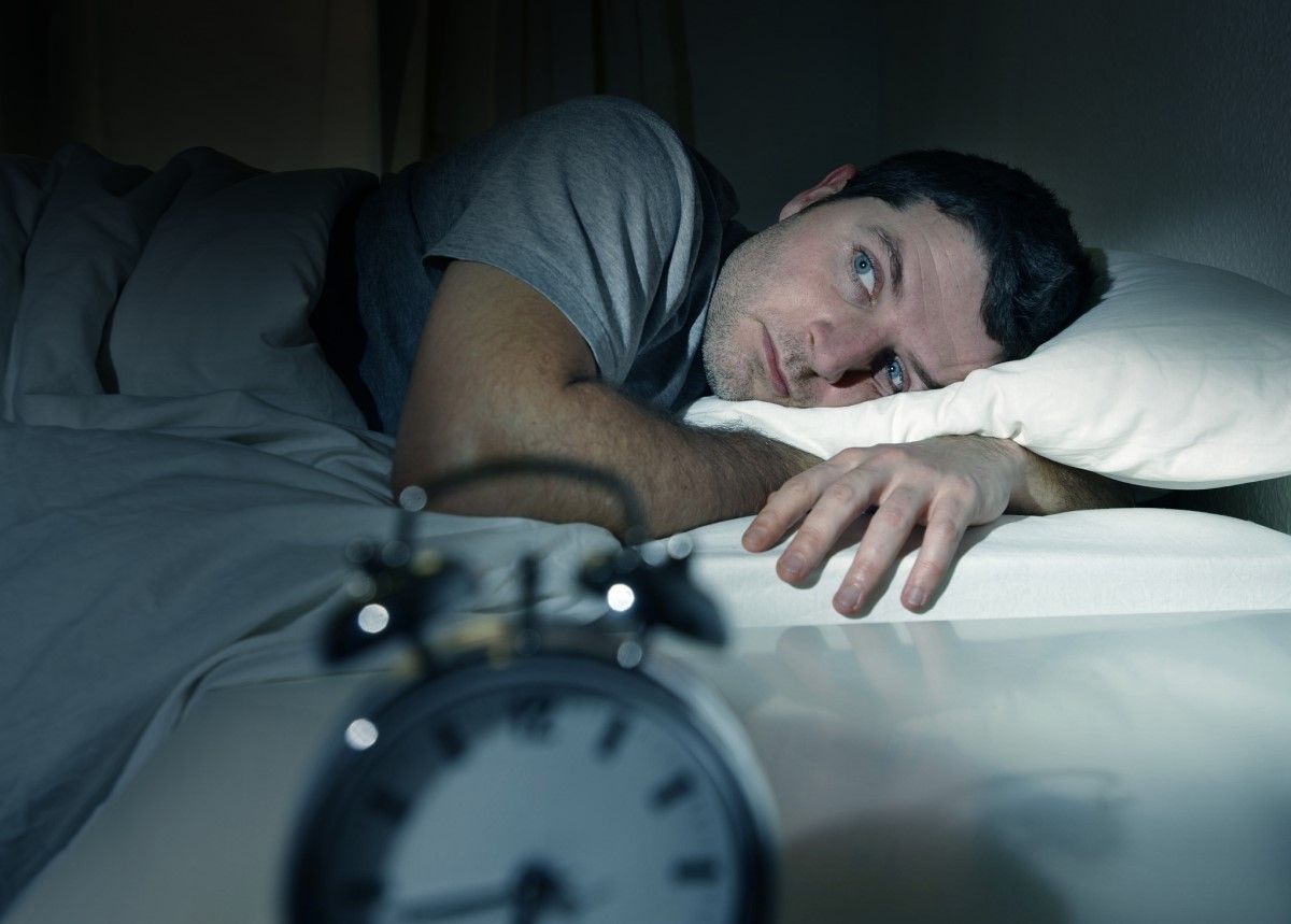 Troubles du sommeil, homme couché dans son lit tard dans la nuit et incapable de s'endormir, horloge sur la table