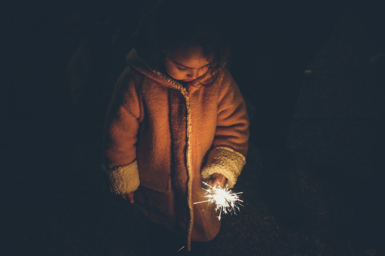 une petite fille vêtue d'un manteau et tenant un cierge magique à la main, regardant tristement le sol