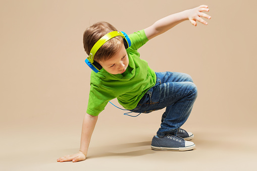 Un enfant en chemise verte avec des écouteurs fait du break dance.