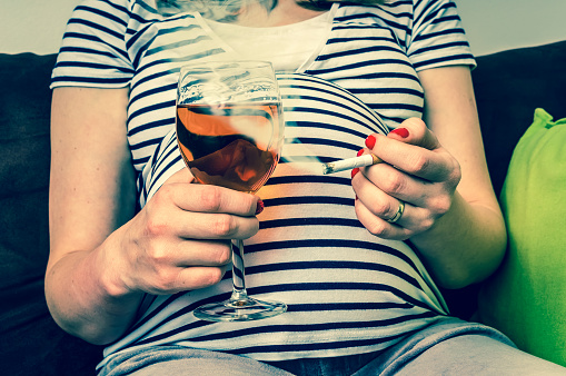 Femme enceinte en T-shirt rayé avec une cigarette et un verre de vin