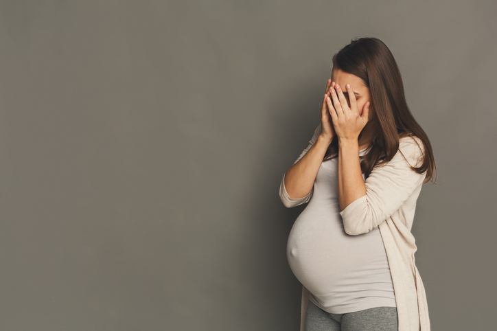 Une femme enceinte fatiguée, se couvrant le visage de ses mains.