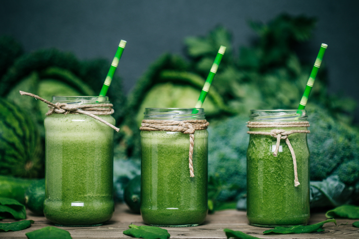 Smoothie aux légumes verts, trois verres, chou, brocoli et petits pois en arrière-plan