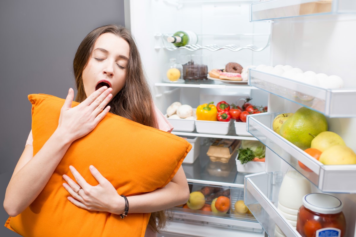 Une femme dormant à côté d'un réfrigérateur, illustrant l'influence des habitudes alimentaires sur la qualité du sommeil.