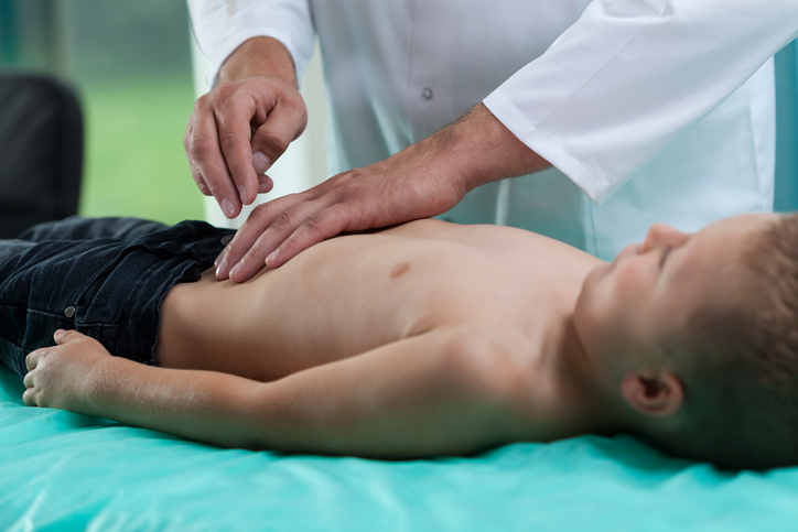 L'enfant est allongé sur la table d'examen, le médecin examine son abdomen, il a mal.