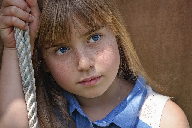 une jeune fille assise sur une balançoire, au regard neutre, aux yeux bleus