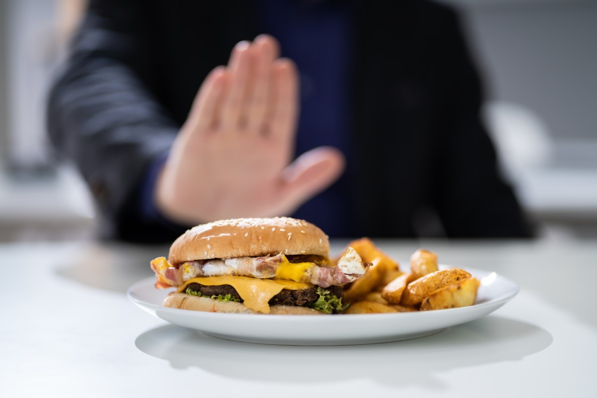 L'alimentation inappropriée comme cause de brûlures d'estomac - un hamburger sur une assiette qu'un homme refuse