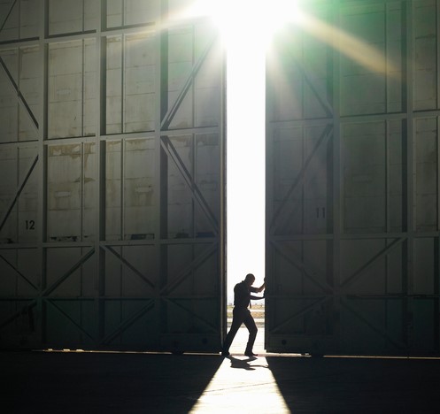 Un homme sort du hall sombre et entre dans la lumière crue, le soleil brille, il ouvre une porte dans le hall.