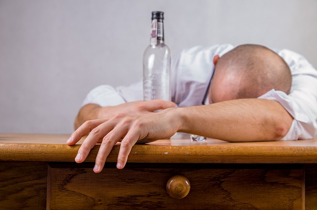 L'alcoolisme est à l'origine des troubles de l'humeur, un homme est allongé sur une table et tient une bouteille d'alcool vide, un alcoolique...