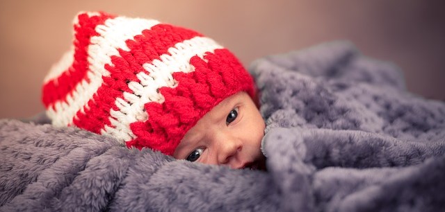 Un enfant, couché et couvert, coiffé d'un bonnet rayé rouge et blanc