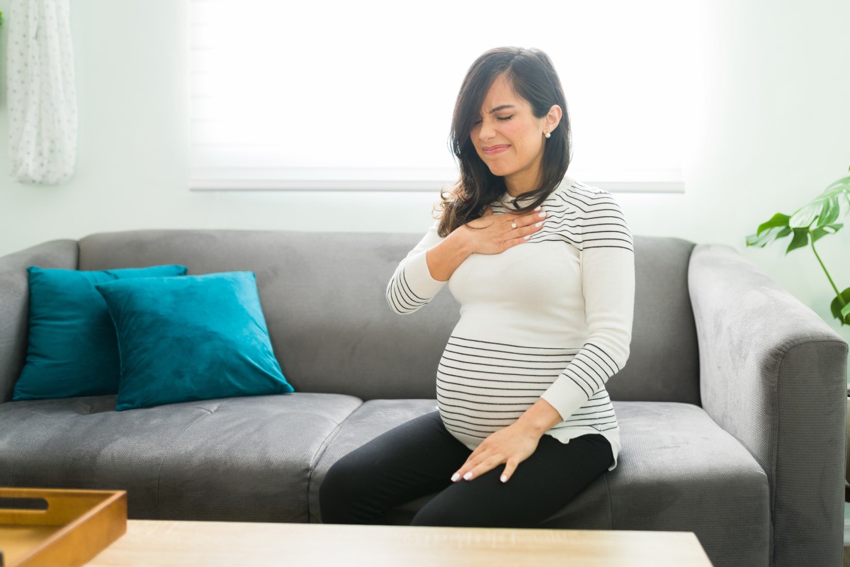 Les brûlures d'estomac sont fréquentes chez les femmes enceintes - une femme enceinte s'assoit sur un canapé et se tient la poitrine.