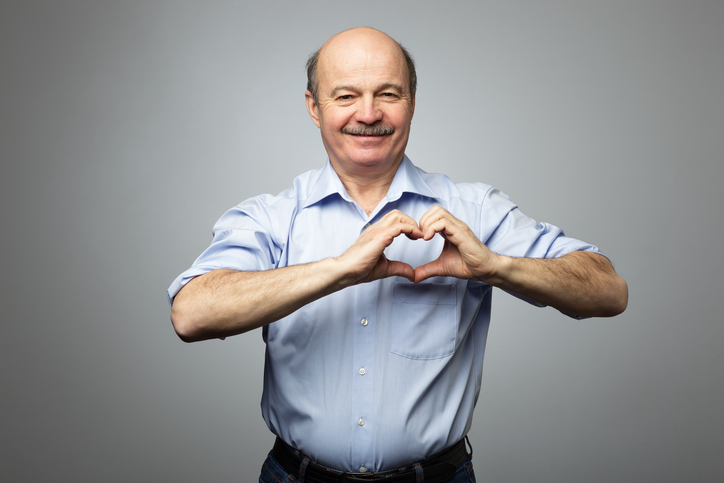 L'homme plus âgé a les mains sur la poitrine en forme de cœur, il a une expression joyeuse sur le visage.