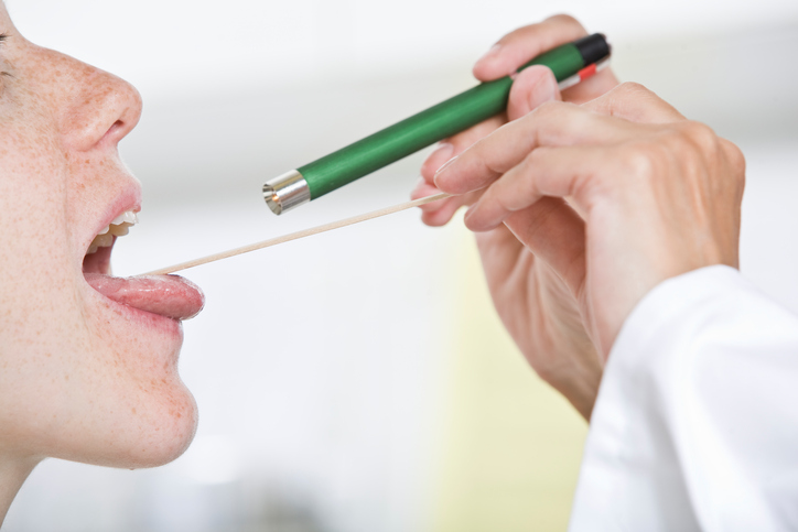 le médecin examine la gorge de la femme à l'aide d'un maillet et de ses yeux, en éclairant la gorge à l'aide d'une lampe de poche