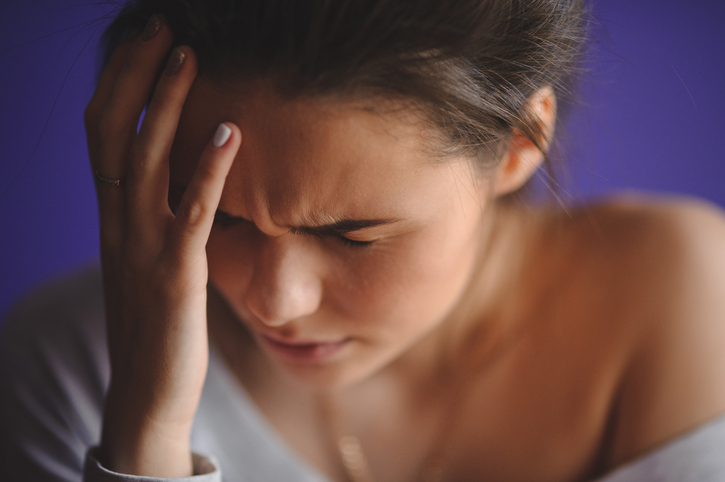 Une femme a mal à la tête et se tient la tête avec les mains.