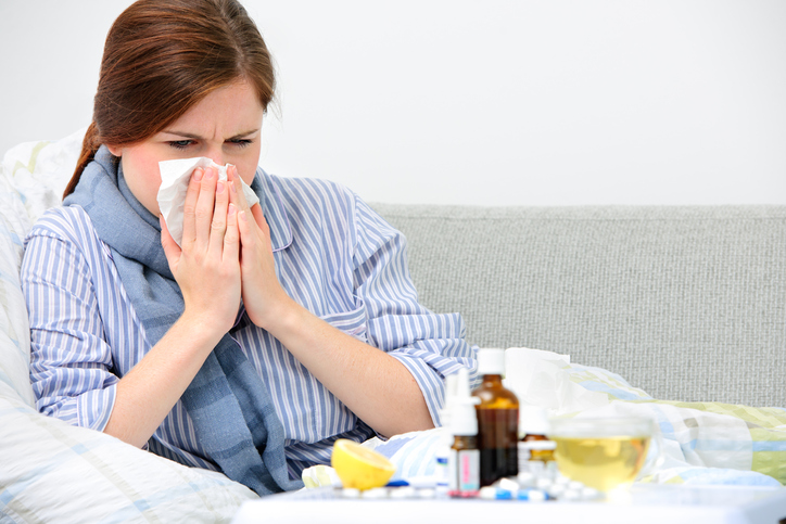 Une femme se nettoie le nez, pour un rhume, qui est la cause de divers maux, dans l'image il y a des médicaments, des pilules, une bouteille, un spray, du citron.